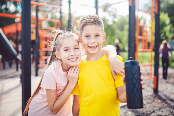 Sportive friends. Brother and sister standing together at street city gym. Children athletes hug smile during workout training. Twins boy and girl posing on playground. Physical development education. - Photo, Image