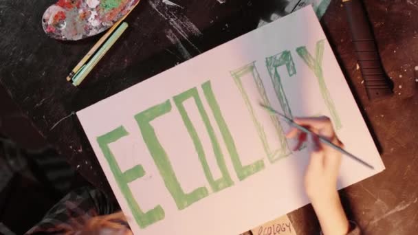 Ragazza Usando vernice verde e pennello per scrivere un segno di ecologia sul manifesto di protesta - Filmati, video