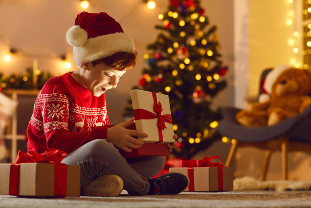 Cheerful boy feeling happy after opening festive gift box with Christmas presents inside - Фото, изображение