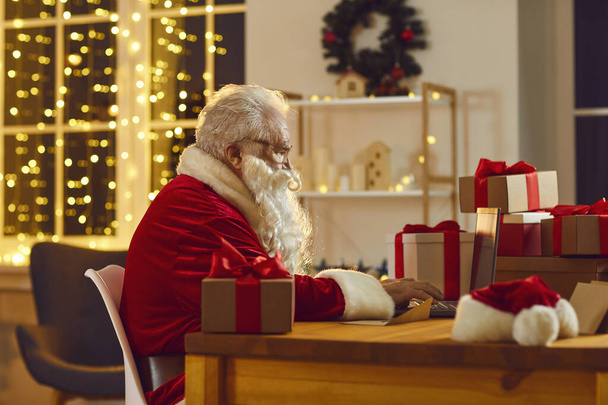 Santa Claus working on his laptop, answering emails and ordering presents delivery online - Fotó, kép