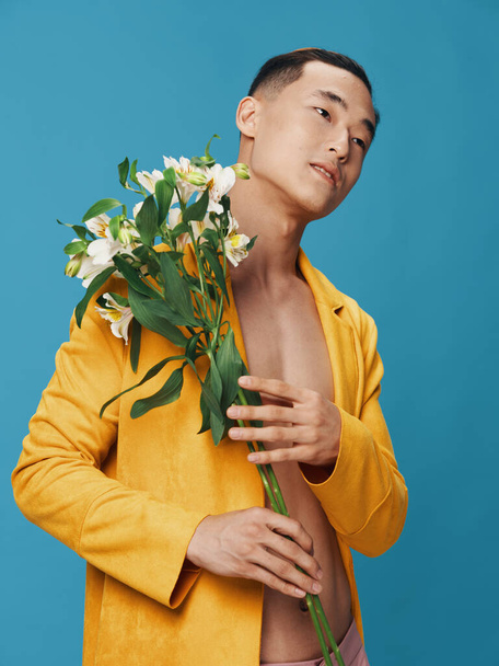 Hombre de ensueño con un ramo de flores y un abrigo amarillo, torso desnudo - Foto, Imagen