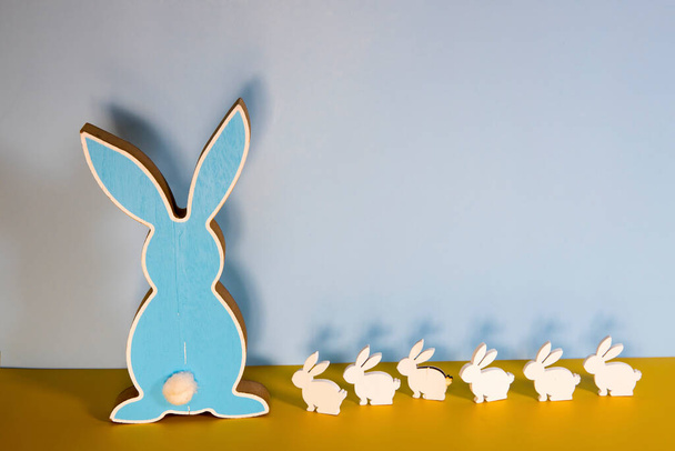 A large flat wooden blue hare and six small whites on a yellow table against a blue wall background. Space for text. Easter concept. Copy space - Фото, зображення