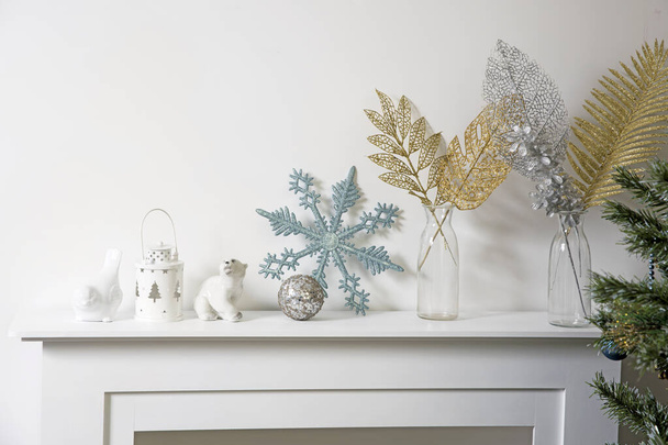 Christmas decoration: blue faux glitter snowflake, candle holder and porcelain white figurine bullfinch bird stand on the console. Copy space. Tropical golden leaves in a transparent bottle - 写真・画像