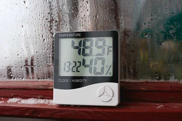 Measurement of air temperature, dew point, humidity with a device (hygrometer), against a background with condensation on the glass, high humidity - Photo, Image