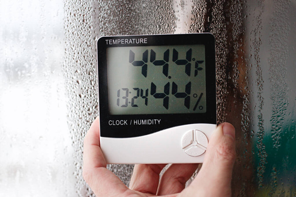 Měření teploty vzduchu, rosného bodu, vlhkosti pomocí zařízení (vlhkoměr), na pozadí s kondenzací na skle, vysoká vlhkost - Fotografie, Obrázek