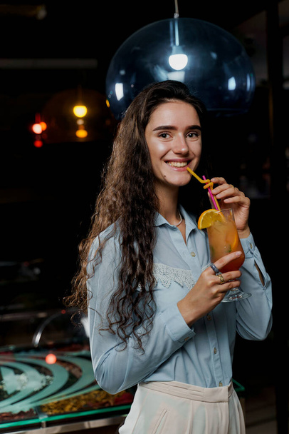 Girl with cocktail is drinking in night club before party. Advert for bar and night clubs. Citrus alcohol drink with orange juice - Fotó, kép