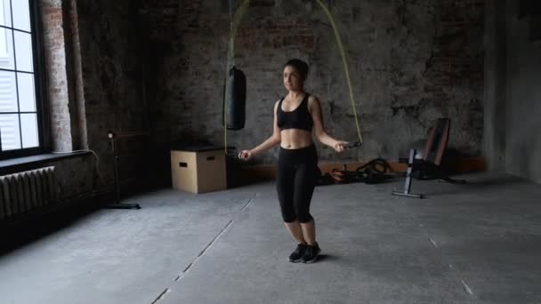 Portrait of fit young woman with jump rope in dark gym. Fitness female doing skipping workout indoors  - Footage, Video
