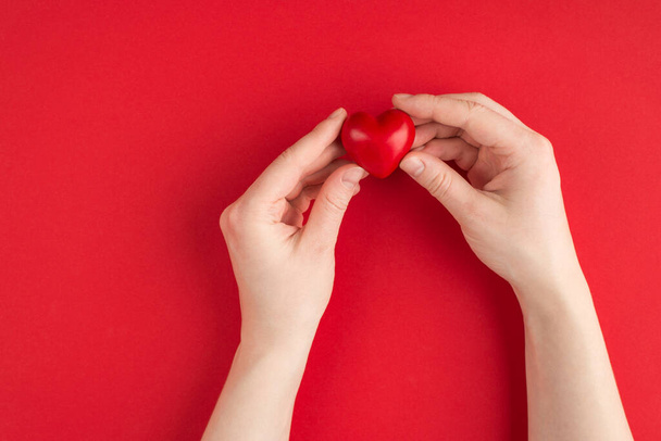 Liebe und Romantik. Oben über der Overhead-Ansicht Foto weiblicher Hände mit rotem Herz auf rotem Hintergrund mit Kopierraum - Foto, Bild