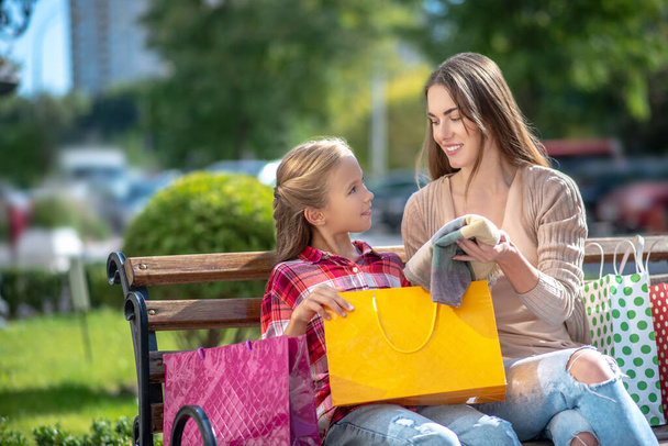 Mom showing her daughter new scarf, sitting on park bench - Foto, imagen