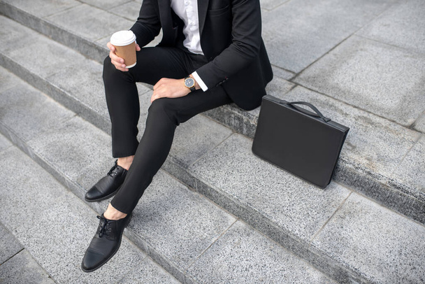 Close up of a man in black suit with a coffee cup in hand - Foto, afbeelding