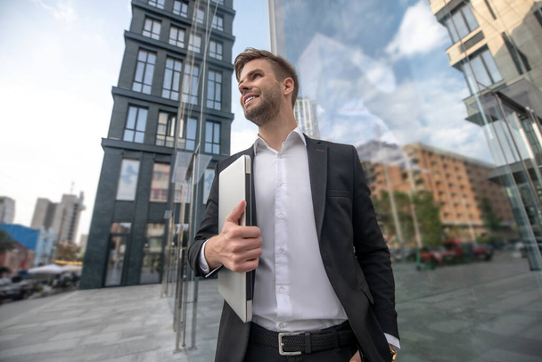 A young man in black suit standing outside and holding laptop - Foto, Bild