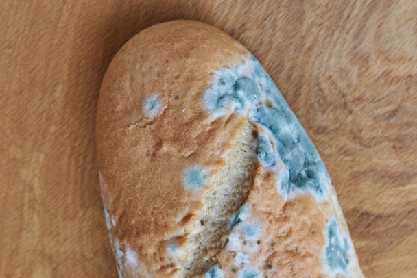 Schimmeliges verdorbenes Brot auf einem hölzernen Hintergrund. Unsachgemäße Lagerung von Lebensmitteln. - Foto, Bild