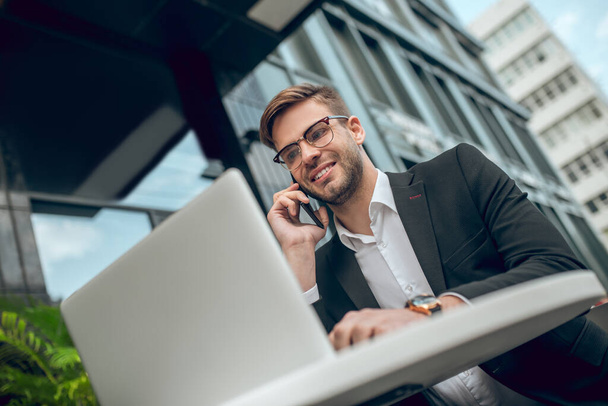 Young businessman in eyeglasses talking on the phone and smiling - Foto, Imagem