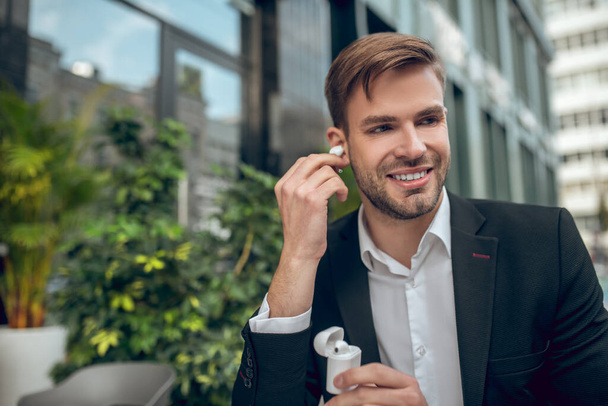 Handsome man wearing wireless headphones and looking contented - Foto, Imagen
