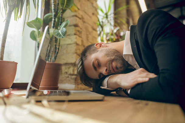 Joven hombre de negocios con una chaqueta negra durmiendo en un café cansado después del trabajo - Foto, imagen