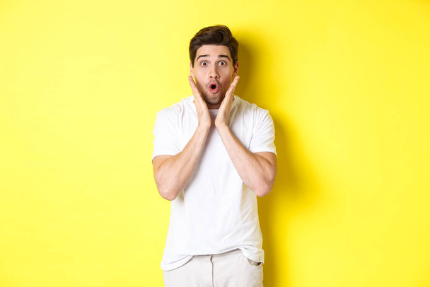 Image of handsome man looking surprised, gasping and saying wow, looking at promo offer amazed, standing over yellow background - Foto, immagini