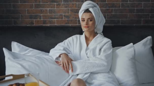 женщина в белом полотенце смотрит в камеру возле подноса с завтраком на кровати - Кадры, видео