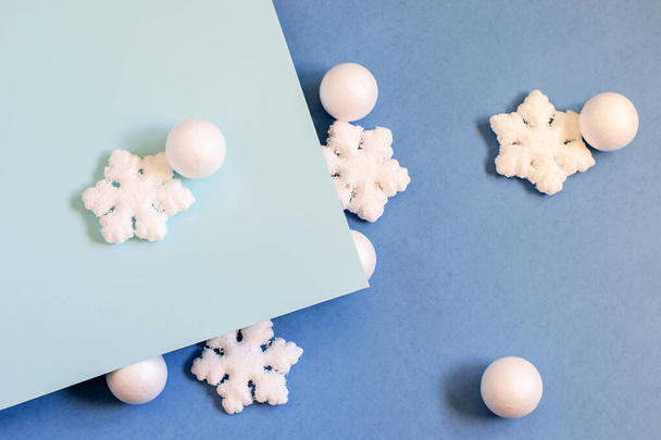 White balls and snowflakes on the bicolor blue paper background. Modern Christmas idea, flat lay, top view. - Photo, Image