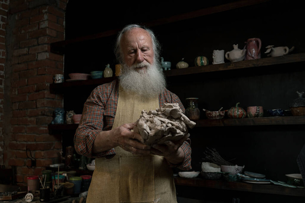 Reconstruction of an ancient craft. An artisan wrinkles clay to create pottery. Holds a lump of clay in his hand. Teaches pottery art. Shows how to sculpt. Dressed in an old outfit. - Фото, изображение