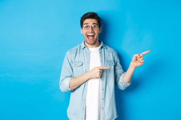 Meglepett férfi szemüvegben pont a másolótérre mutat, bemutatja promo ajánlat kék háttér, álló felett kék háttér - Fotó, kép