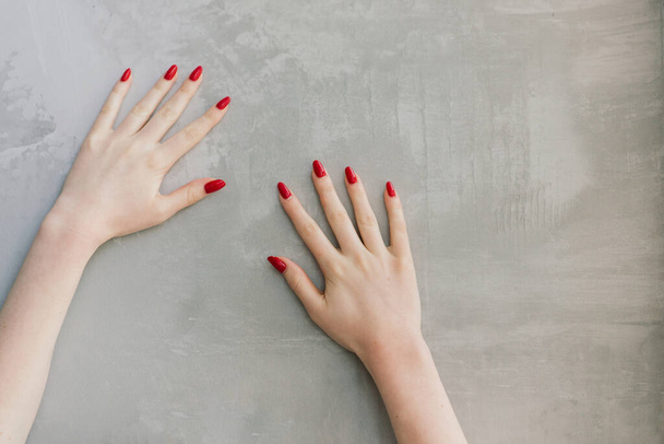 Ізольовані жіночі руки з червоними цвяхами перед сірою стіною
 - Фото, зображення