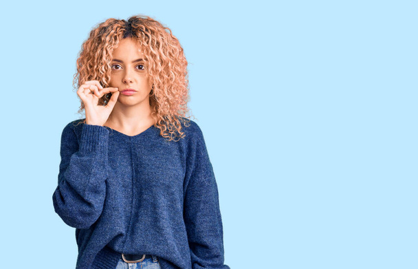 Young blonde woman with curly hair wearing casual winter sweater mouth and lips shut as zip with fingers. secret and silent, taboo talking  - Photo, Image