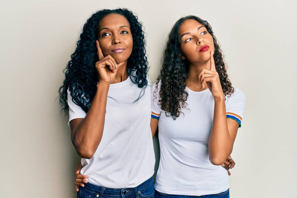 Afrika kökenli Amerikalı anne ve kız günlük beyaz tişört giyerek ciddi bir yüz ifadesiyle eli çenesinde soru sorarak kafa karıştırıcı fikirleri düşünürler.  - Fotoğraf, Görsel