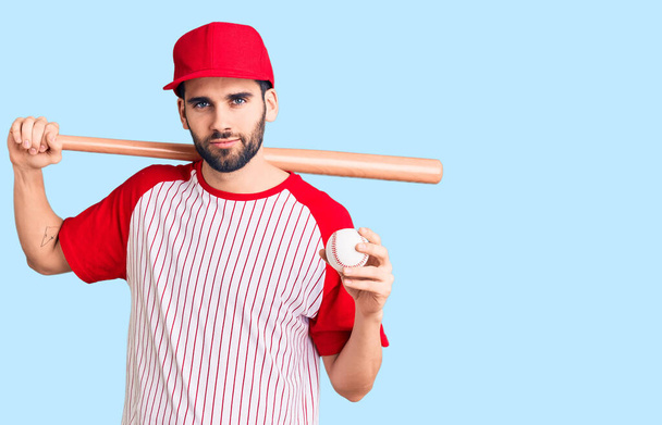 Молодий красивий чоловік з бородою грає в бейсбол, тримає кажан і м'яч мислення ставлення і тверезий вираз, дивлячись на себе впевнено
  - Фото, зображення