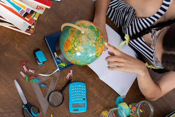 The schoolgirl finds places on the globe and writes them down as a destination for her next vacation. The best student in school. - Foto, imagen
