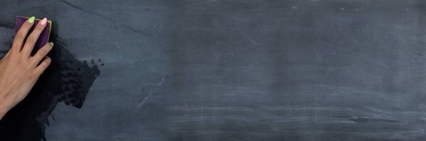 Panoramic frame for a womans hand wiping the blackboard with a wet sponge before the next lessons in the classroom. Prepares a place for writing on a school blackboard. - Zdjęcie, obraz