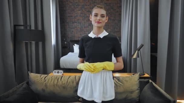 allegra governante in uniforme e guanti di gomma in piedi in camera d'albergo - Filmati, video