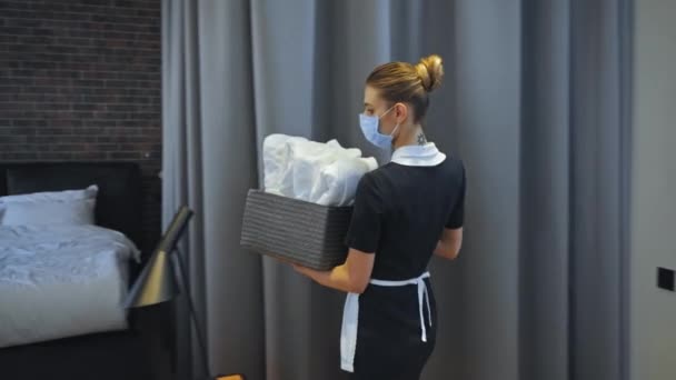 giovane cameriera in maschera medica che trasporta scatola con asciugamani puliti  - Filmati, video
