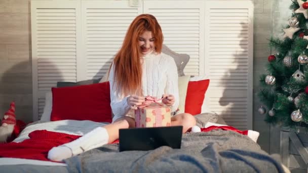 Mujer feliz se sienta en la cama en casa y sonríe mientras se comunica en línea a través de la computadora portátil - Metraje, vídeo
