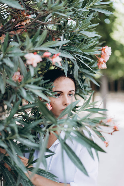 Lifestyle. Portrait of a beautiful young woman in a white shirt is covered with leaves and pink flowers. - Foto, Bild