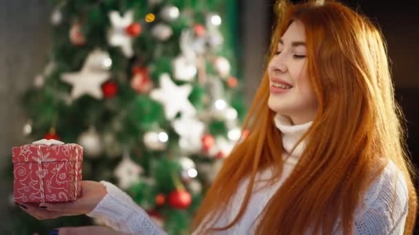 Όμορφη ευτυχισμένη κοκκινομάλλα γυναίκα κάθεται φόντο Χριστουγεννιάτικο δέντρο και χαμογελώντας - Πλάνα, βίντεο