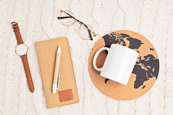 Mockup with white mug, glasses, watch, pen, notebook and globe print on white knitted background. Stylish accessories for office or travelling concept. Flat lay, top view - 写真・画像