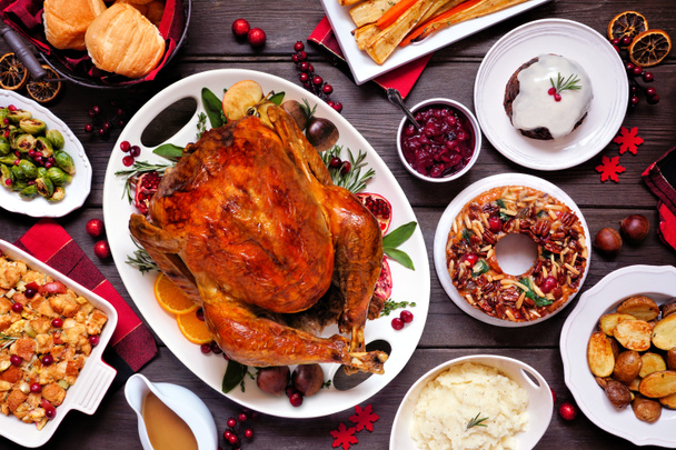 Traditional Christmas turkey dinner. Top view table scene on a dark wood background. Turkey, potatoes and sides, dressing, fruit cake and plum pudding. - Foto, imagen