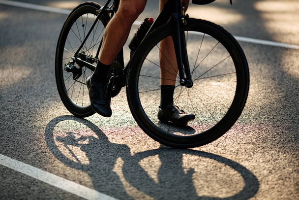 Spor ayakkabılı güçlü erkek bacakları asfalt yolda bisiklet sürüyor. Aktif giyimli bir adam temiz havada en sevdiği hobiyi yapıyor.. - Fotoğraf, Görsel