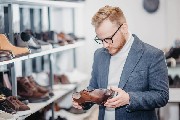 stilista maschile alla moda in occhiali e una giacca sceglie scarpe nel negozio. - Foto, immagini