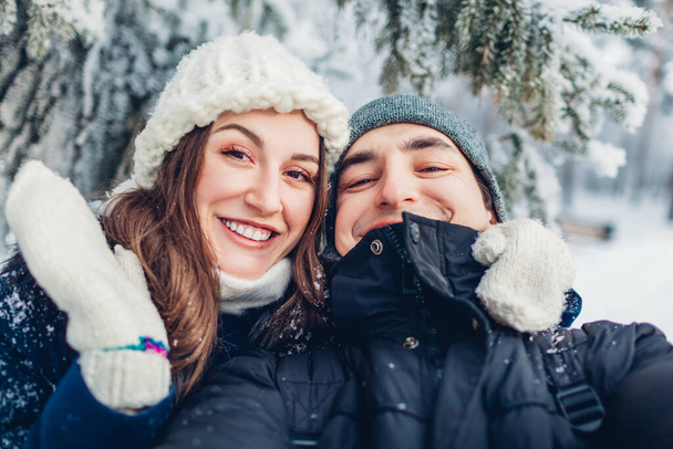 Verliefd stel die selfie nemen en knuffelen in besneeuwd winterbos. Jonge gelukkige mensen die plezier hebben buiten te lopen. Valentijnsdag - Foto, afbeelding