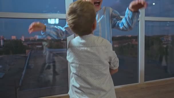 alegre hermano levantando hermana cerca de ventanas panorámicas en casa - Metraje, vídeo