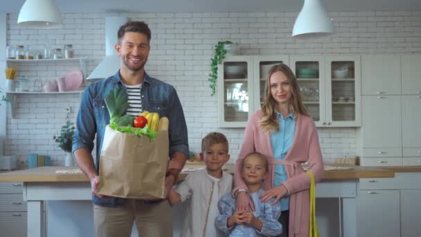 Mosolygó család bevásárló táskák nézi kamera a konyhában - Felvétel, videó