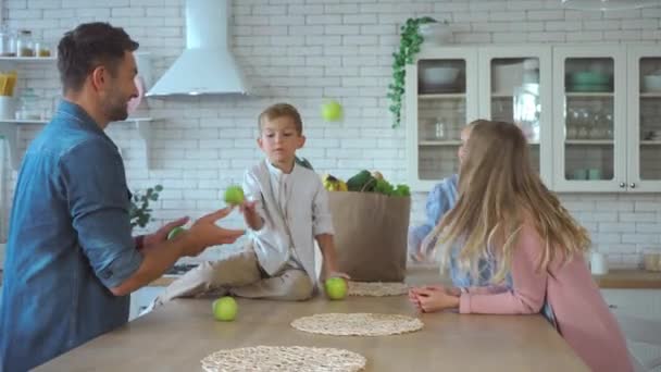 Χαμογελώντας πατέρας ζογκλέρ με πράσινα μήλα, ενώ η οικογένεια χειροκροτεί στην κουζίνα - Πλάνα, βίντεο