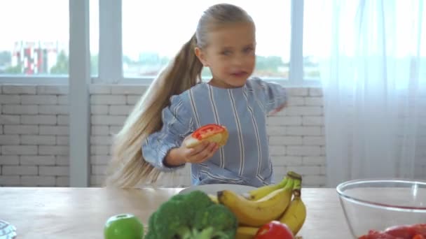 Fröhliches Mädchen redet und gestikuliert beim Sandwich essen am Tisch in der Küche - Filmmaterial, Video