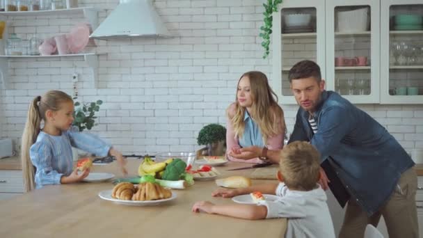 Tochter zeigt mit der Hand auf Sandwiches, während Eltern in Küche reden - Filmmaterial, Video