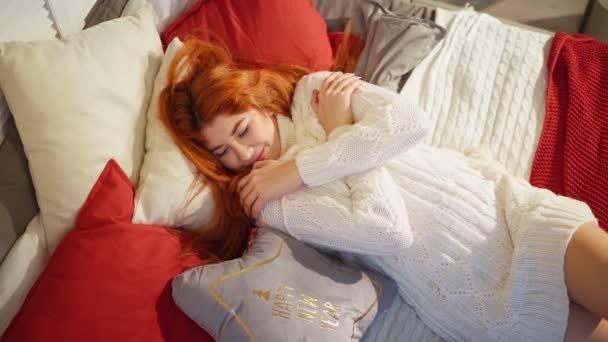 Kényelmes, szexi, vörös hajú nő fehér kötött pulóverben fekszik a kanapén. Boldog új évet! - Felvétel, videó