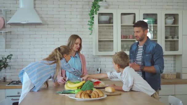 Sonriente familia hablando mientras sirve mesa durante el desayuno en la cocina - Metraje, vídeo