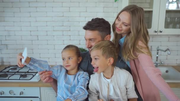 Hija feliz con teléfono inteligente hablando selfie con la familia en la cocina - Imágenes, Vídeo