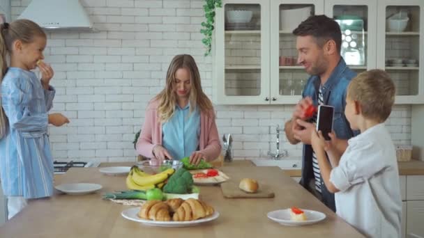 Γιος με smartphone λήψη φωτογραφιών της οικογένειας προετοιμασία πρωινό στην κουζίνα - Πλάνα, βίντεο