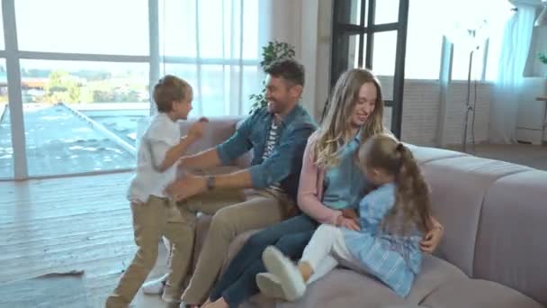 Cheerful sibling jumping on couch and having fun with parents in living room - Footage, Video
